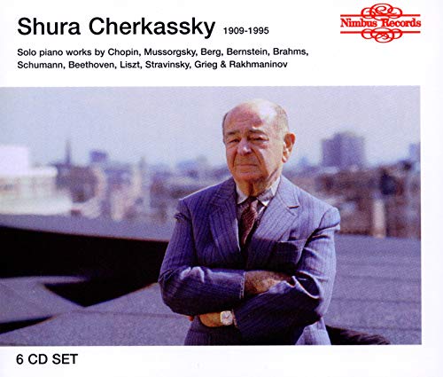 Shura Cherkassky in a suit with arms crossed, against a city skyline background.