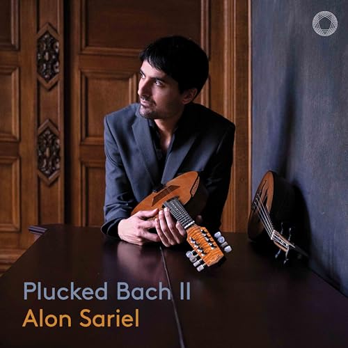 Alon Sariel in a suit holding a mandolin, with another instrument nearby.