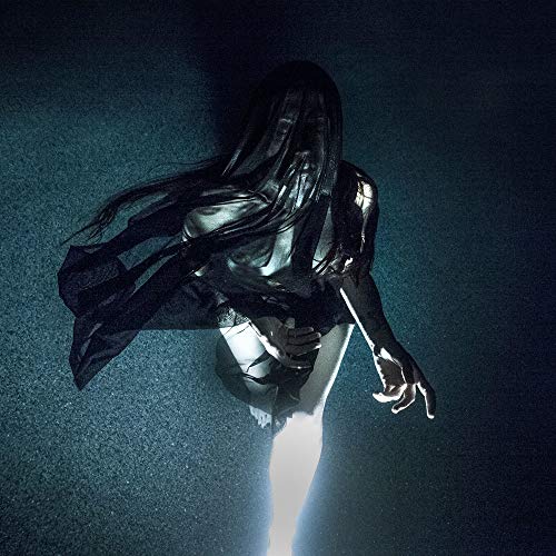 Dark, shadowy figure with long hair, draped in fabric, against a blue background.