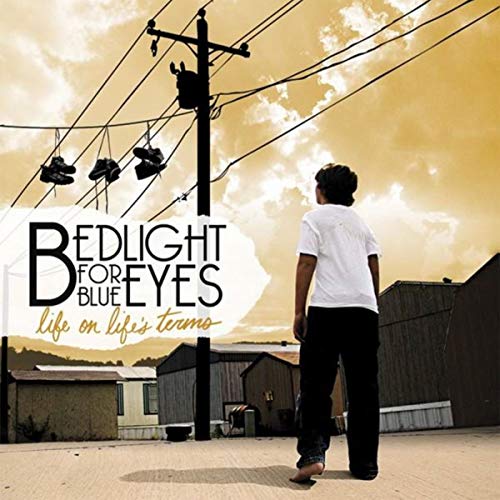 CD cover: person looking at buildings with shoes hanging from wires.