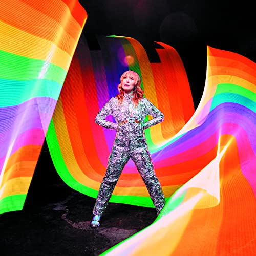 Woman in silver suit stands before colorful light streaks.