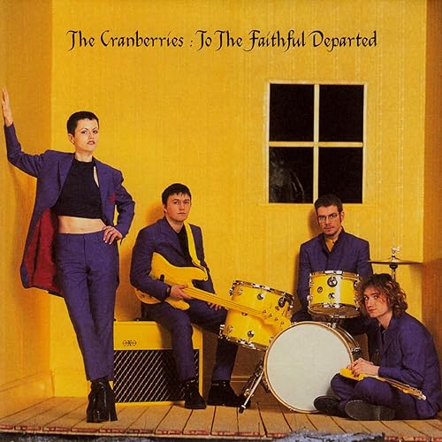 The Cranberries band members posed in front of a yellow wall.