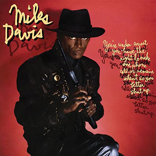 Miles Davis in a hat and jacket, red background with text.