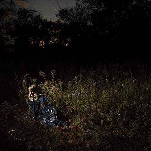 Woman in reflective clothing sits among dark foliage at night.