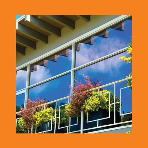 Building facade with window reflecting clouds and flowering plants.