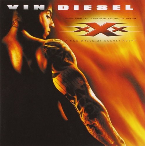 Vin Diesel with a tattooed arm against a fiery orange and black background.