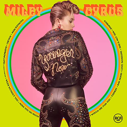 Miley Cyrus wearing a rhinestone-studded leather jacket and pants against a pink circular background.