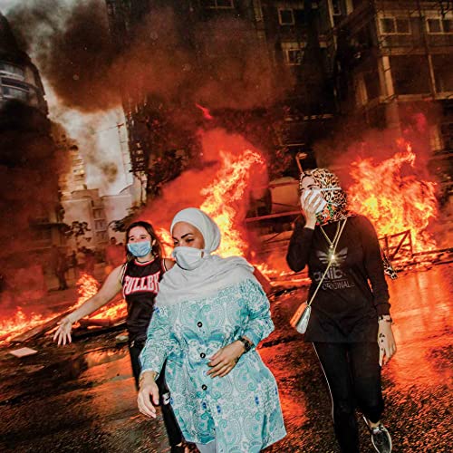 Women wearing masks walk past burning debris in a city street.