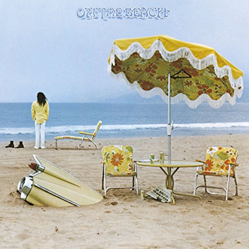 Beach scene with a person, umbrella, chairs, and vintage car.