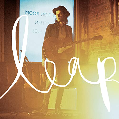 James Bay wearing a hat and holding a guitar with the word Leap written.