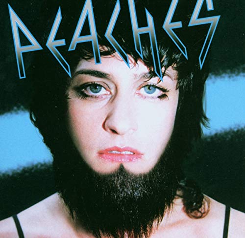 Close-up portrait of Peaches with a dark beard against a blue and black background.