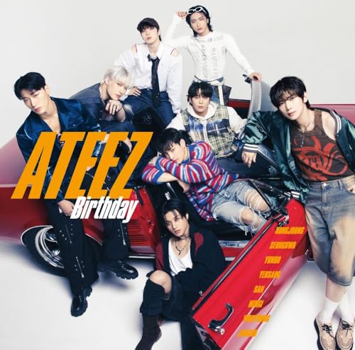 The seven members of Ateez pose around a red vintage car against white background.