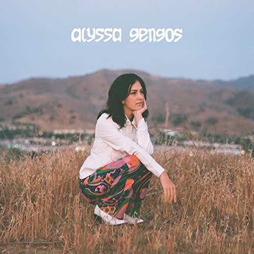Woman crouching in a field with mountains in the background.