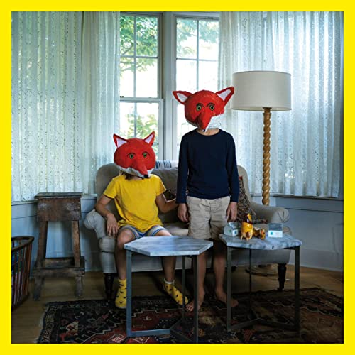 Two people wearing fox masks sit in a living room.