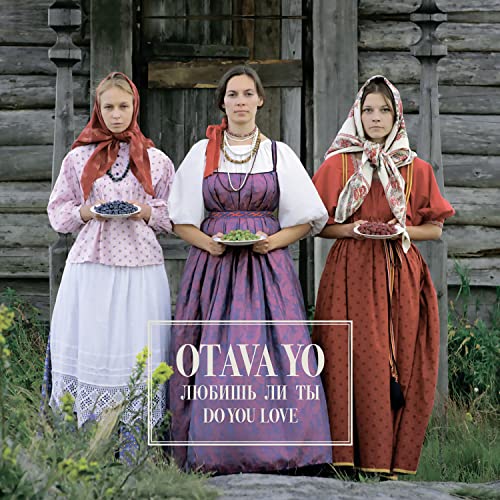 Three women in traditional clothing holding berries in front of a wooden building.