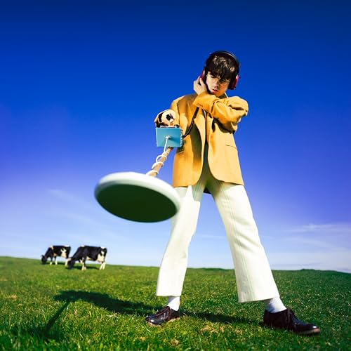 Man in tan suit holds metal detector in a green field.