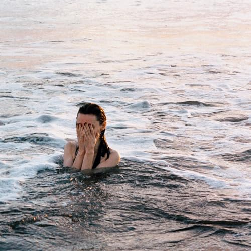 Woman with face covered by hands immersed in rippling water.