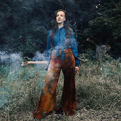 Woman with guitar in a field, smoke swirling around her.
