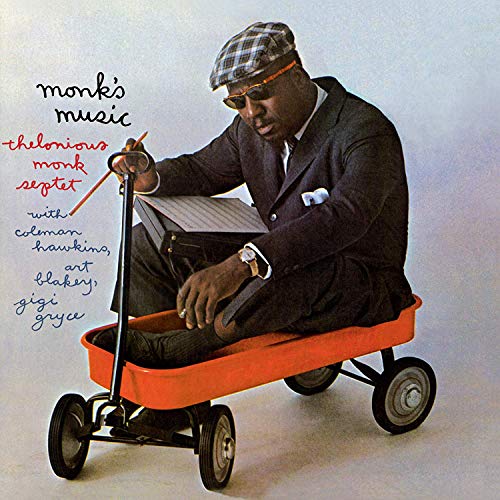 Thelonious Monk wearing a hat and sunglasses, sitting in a red wagon holding music.