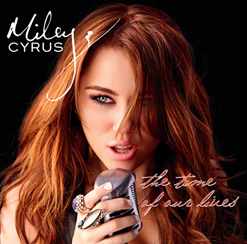 Miley Cyrus holding a microphone with long red hair and several rings on her hand.