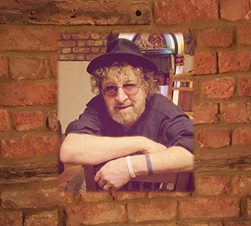 Man with beard and hat framed by a brick wall.