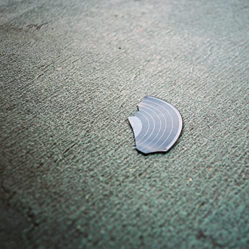 A small, broken fragment of a vinyl record lying on a textured gray surface.