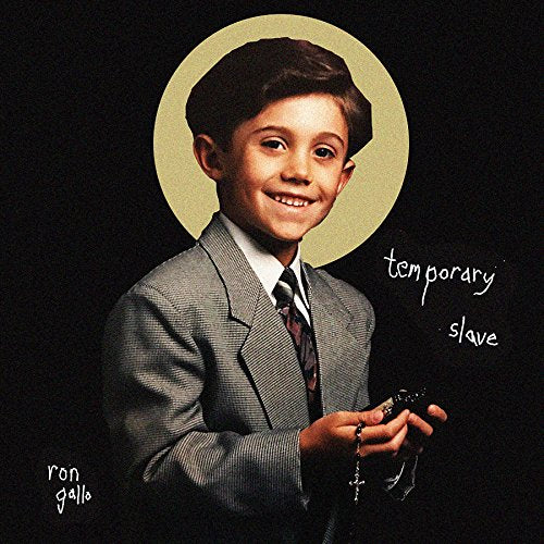 A smiling boy in a suit holds a rosary against a black background.