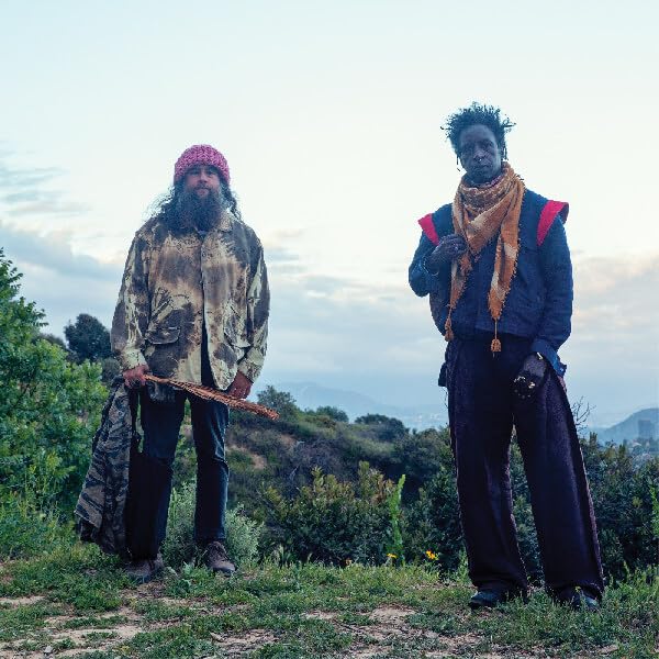 Two men, Saul Williams and Carlos Nino, stand outdoors in natural settings.
