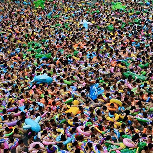 Crowded swimming pool filled with people and colorful inflatable toys.