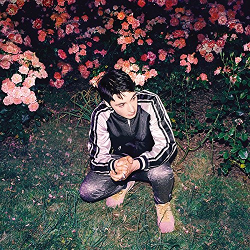 Person crouching amongst pink roses, wearing a black and pink jacket.