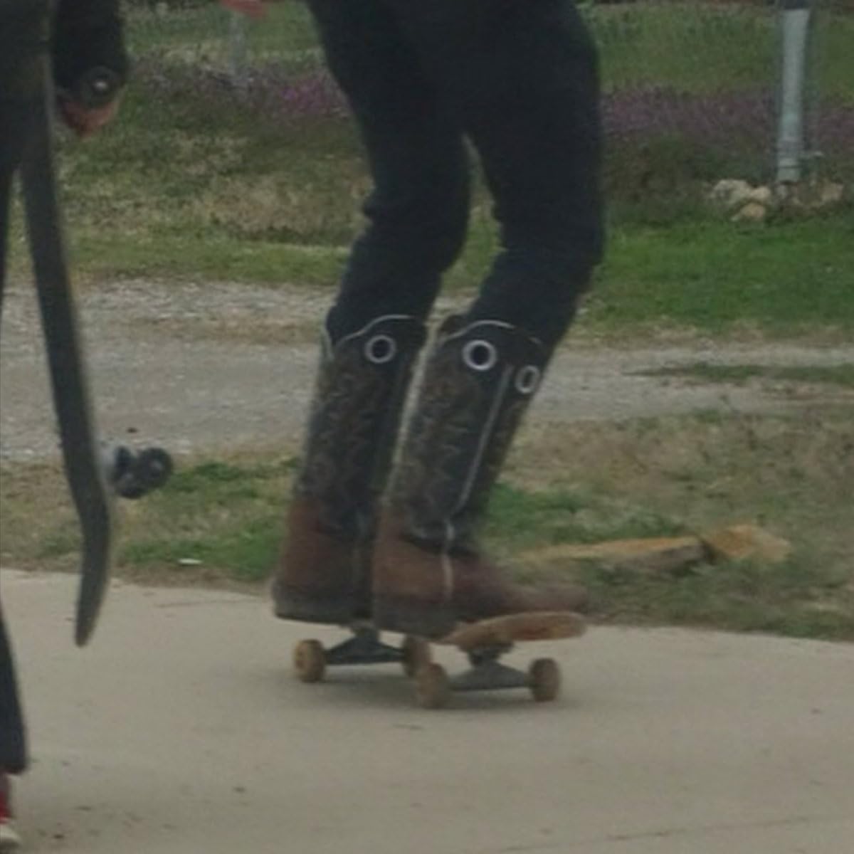 Person in cowboy boots skateboarding outdoors, mid-shot, slightly blurred.
