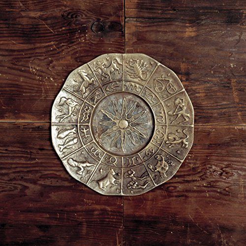 A metallic zodiac plate with a central sun motif resting on a wooden surface.