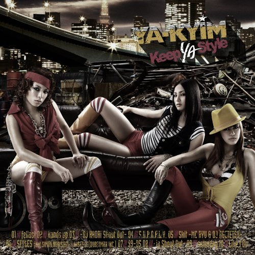 Three women posing on a black leather couch in front of a junkyard background.