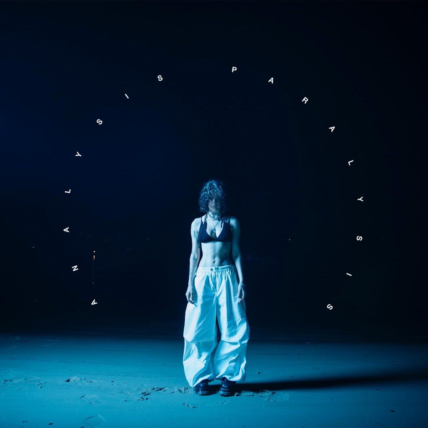 CD cover: woman in baggy pants stands on a dark beach.