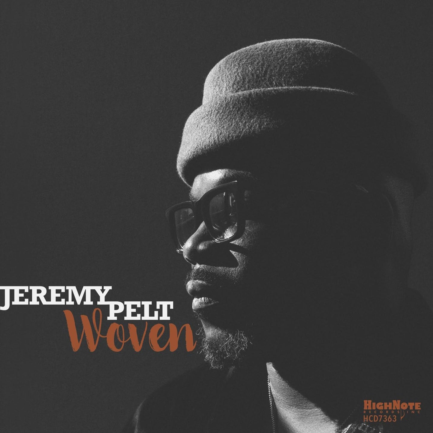 Black and white portrait of jazz trumpeter Jeremy Pelt wearing a cap and glasses.