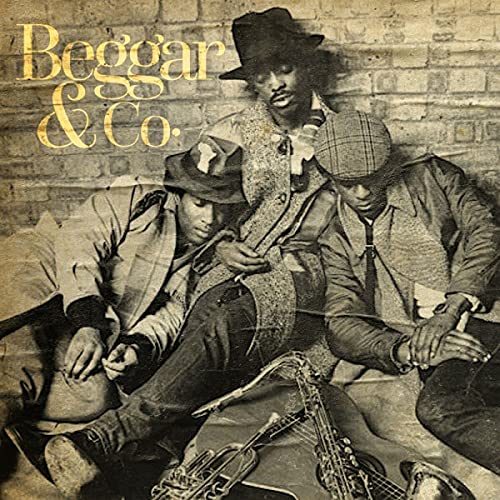 Three musicians with hats and instruments pose against a brick wall.
