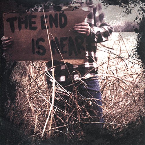 Person holding a weathered sign reading "The End Is Near" outdoors.
