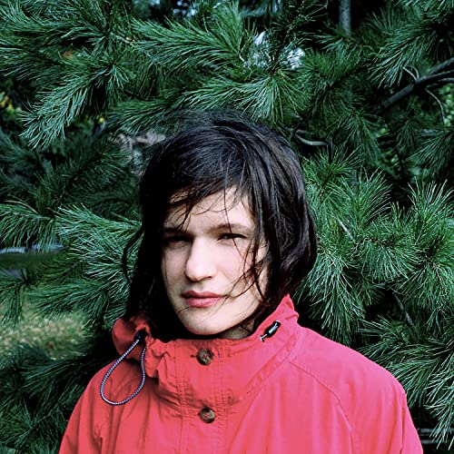 Portrait of a person with dark hair, wearing a red jacket, in front of trees.