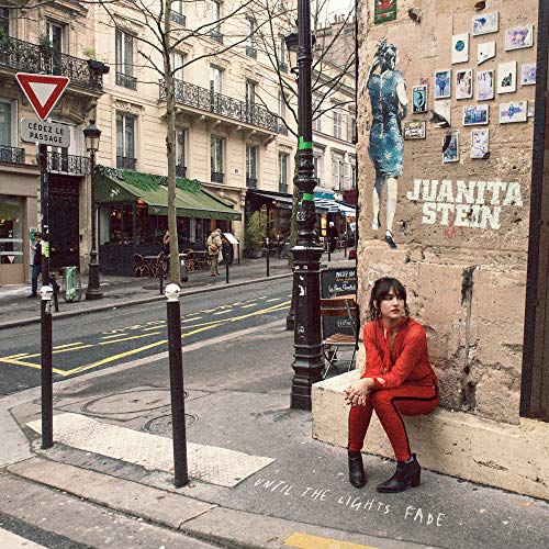 Woman in red sits by a wall with album art and street scene.