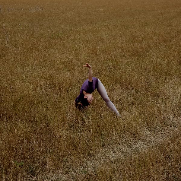 Woman in purple clothing bends backwards in a field of tall grass.