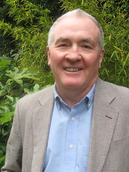 Headshot of a smiling older man in a tweed jacket, outdoors.