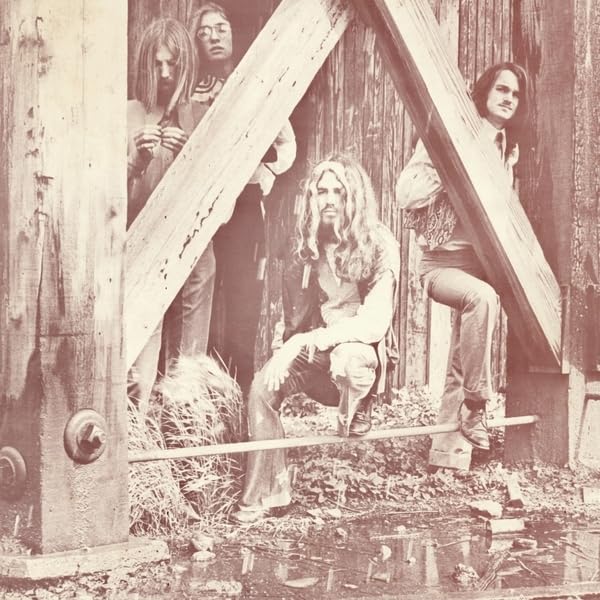Sepia-toned photo of five long-haired men posing near a wooden structure.