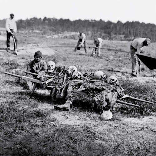 Black and white photo of skulls and bones on a handcart, workers nearby.
