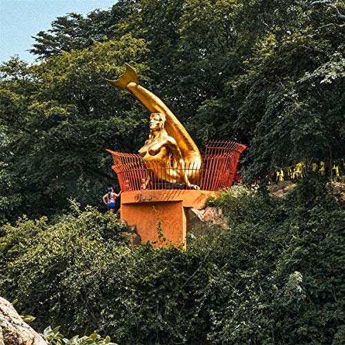 Golden sculpture of a reclining figure atop an orange structure, trees.