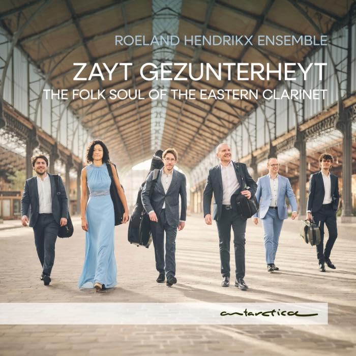 Musical ensemble walking towards the viewer under a train station arch.