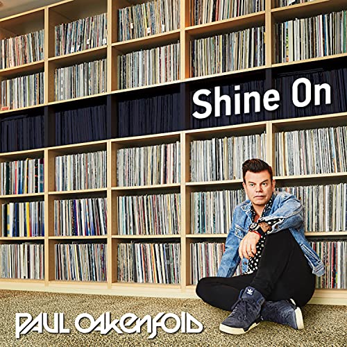 Paul Oakenfold sits before shelves filled with vinyl records; album cover.