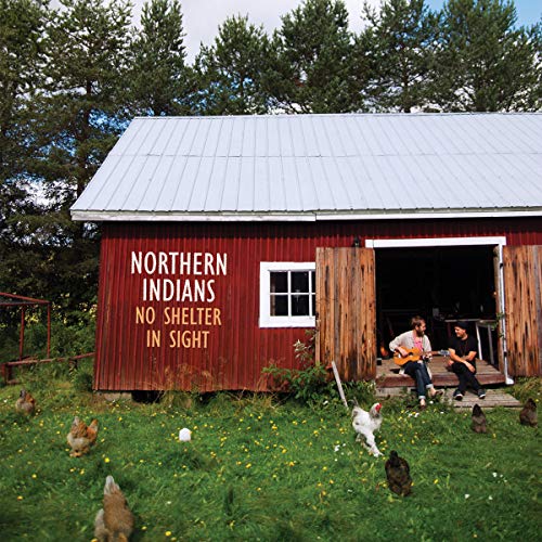 Two men playing guitars outside a red barn with chickens in the grass.