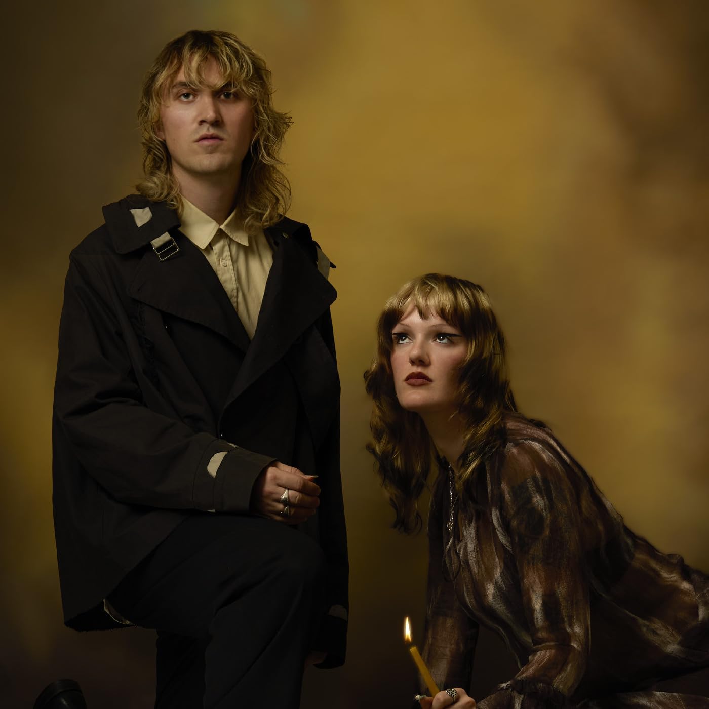 Two people with long hair, one holding a lit candle, studio portrait.