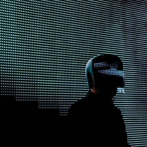 Silhouette of a person wearing a futuristic helmet in front of lights.
