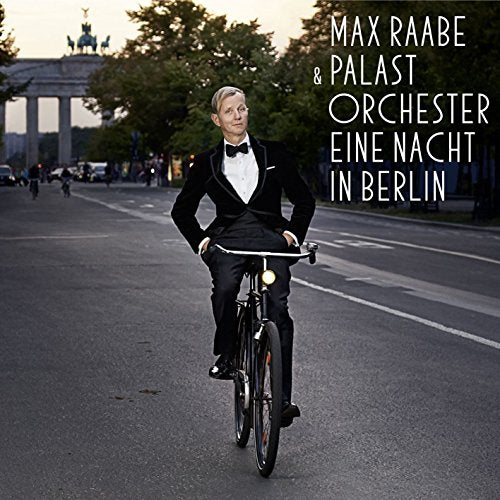 Man in tuxedo on bicycle, Berlin Brandenburg Gate in background.
